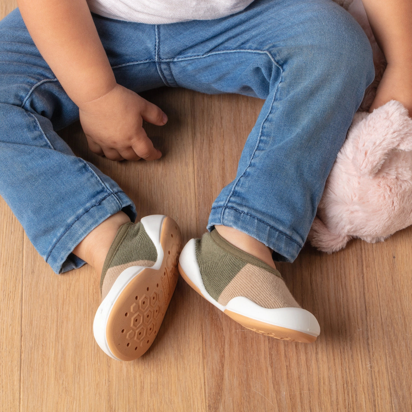 A pair of color block olive baby sock shoes with a white bee hive patterned sole.