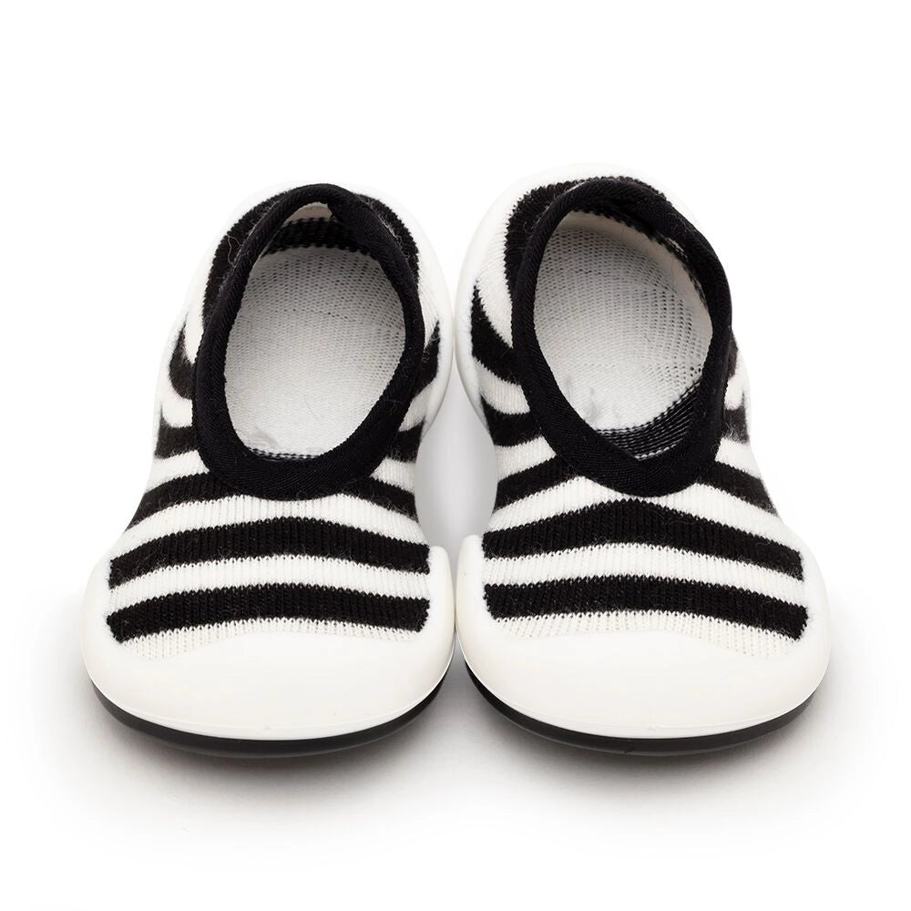 A pair of black and white striped baby sock shoes with a non-toxic, BPA-free, ultra-light rubber sole.