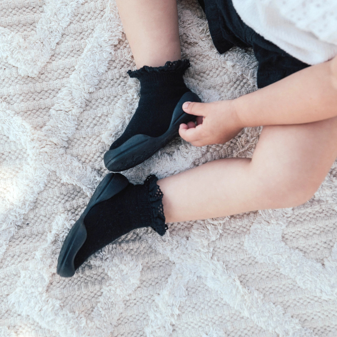A pair of black Komuello First Walker Baby Sock Shoes with lace trim on the top and a non-slip rubber sole.