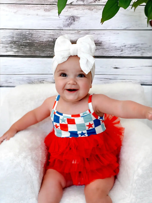 Baby wearing a red and white checkered romper with a large bow on a wooden background