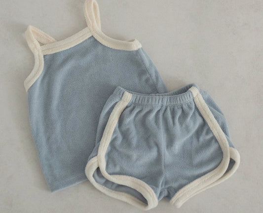 A set of baby beachwear consisting of a blue sleeveless top and beige shorts with a white trim.