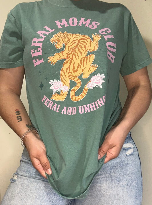 A person wearing a green t-shirt with 'Feral Moms Club' text and a graphic of a tiger and flowers.