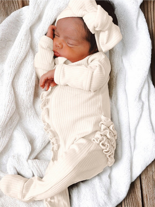 A sleeping infant in a beige organic ribbed frill zip footie with a bow on the hat.