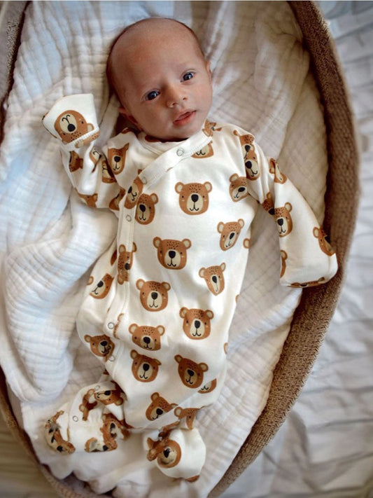 A newborn baby wearing a beige organic gown with bear face patterns, lying inside a basket.
