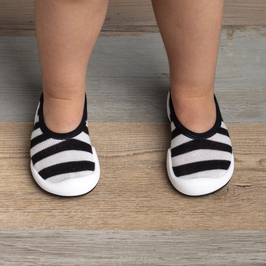 A pair of black and white striped baby sock shoes with a non-toxic, BPA-free, ultra-light rubber sole.