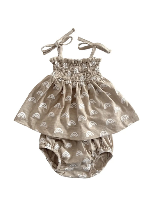 A beige colored baby smocked set with rainbow patterns, consisting of a spaghetti strap top and matching bloomers with adjustable straps.